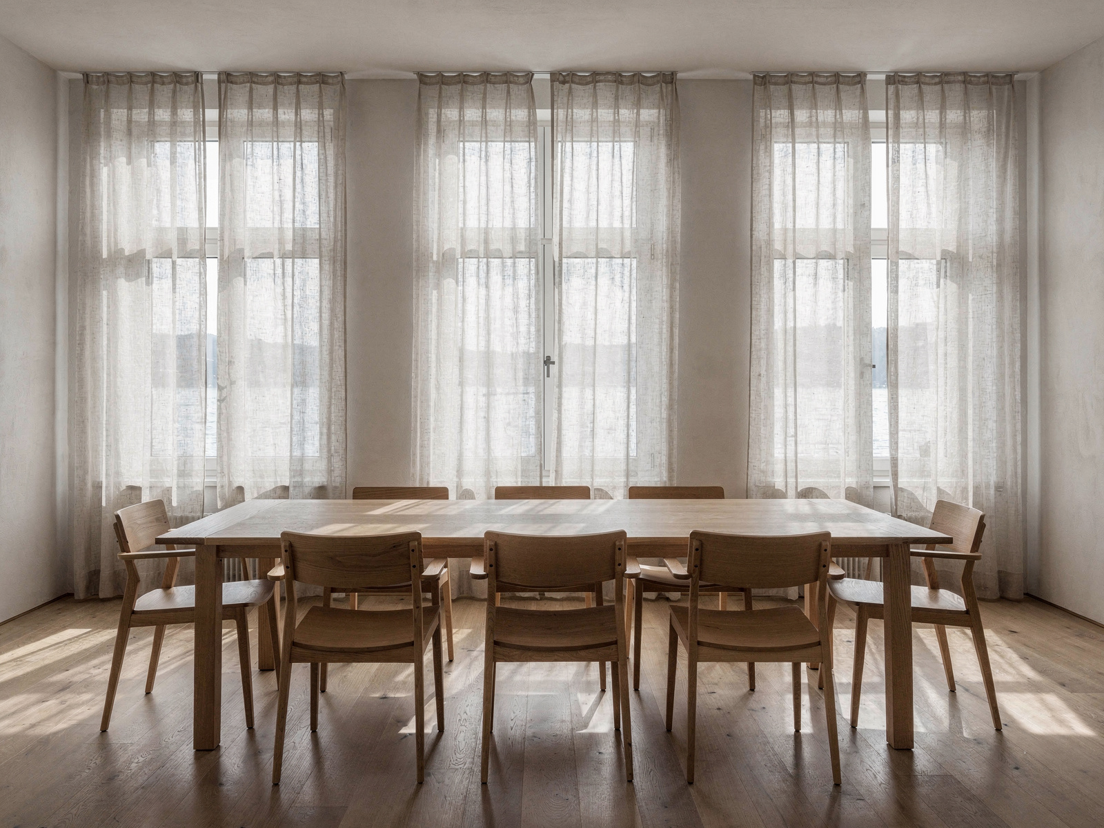 A long wooden table and chairs in a plain, daylit room.