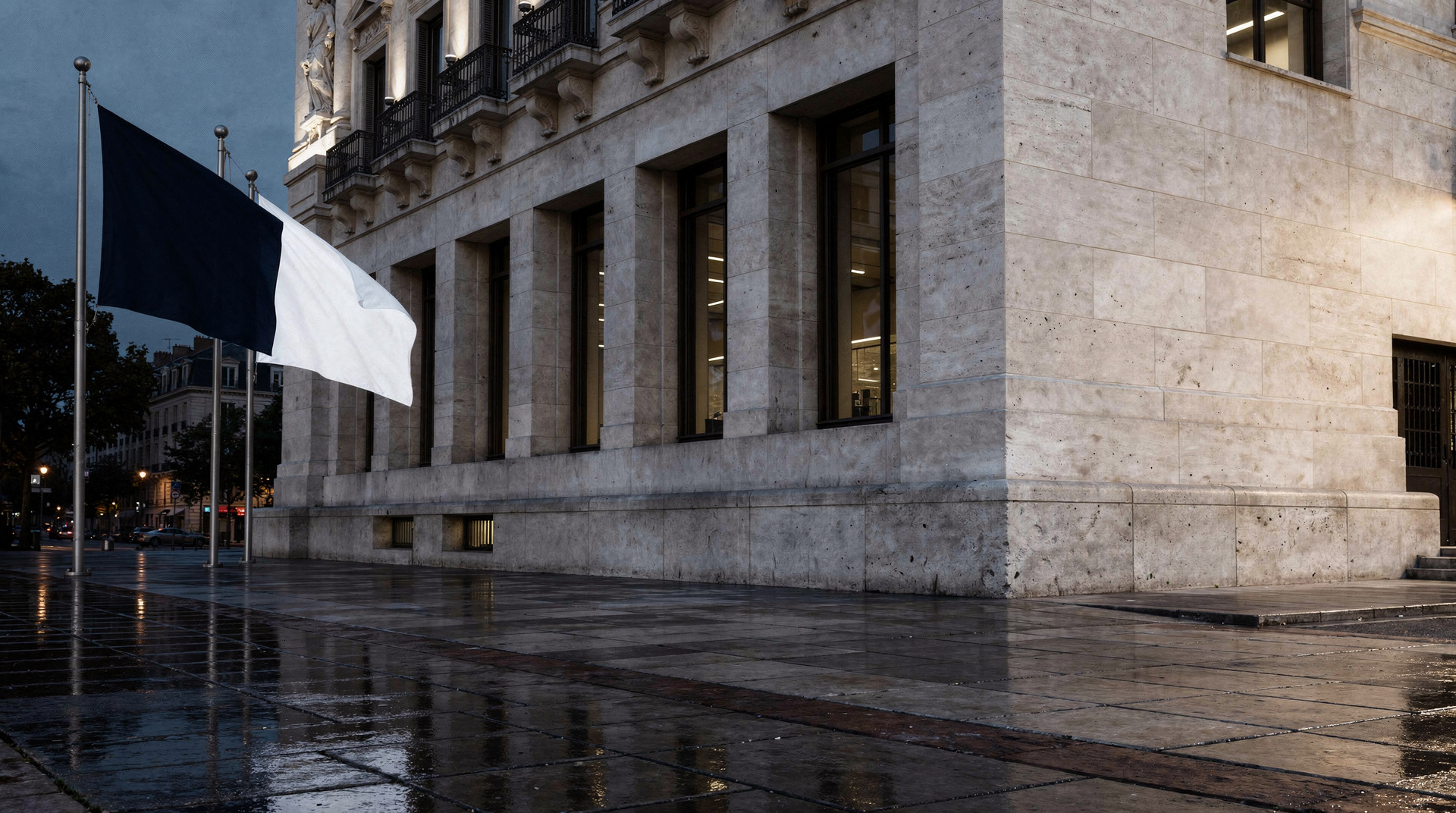 A pale stone façade and wet forecourt in the evening.